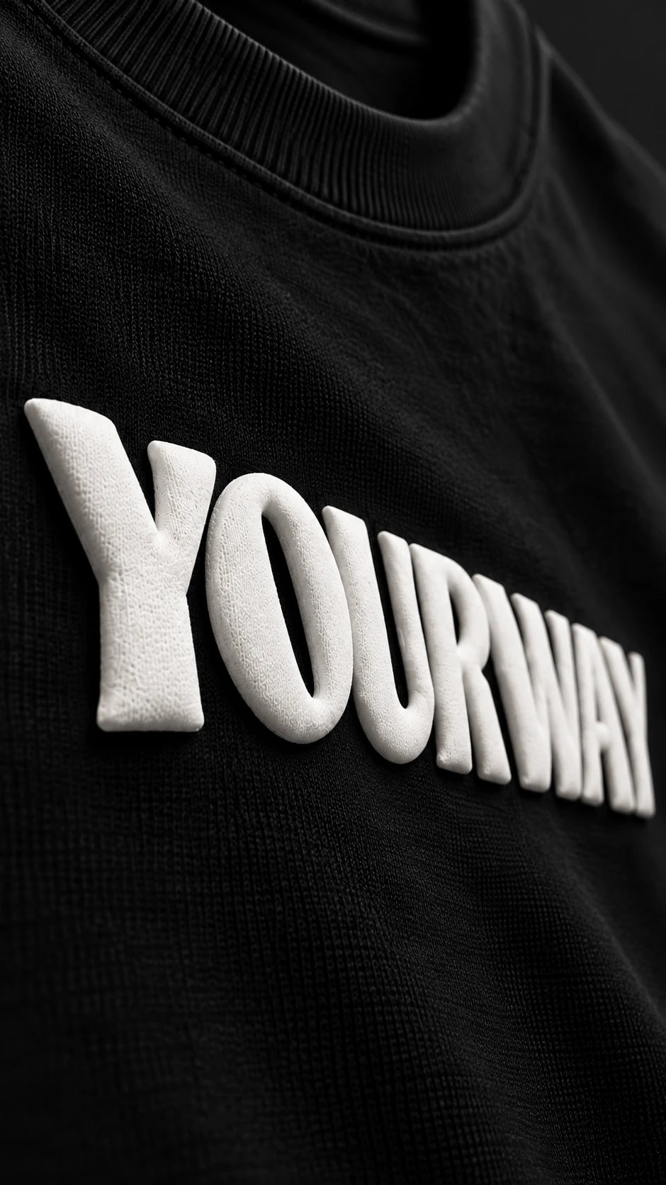 Close-up of the raised white YOURWAY puff print wordmark on the Black T-Shirt fabric
