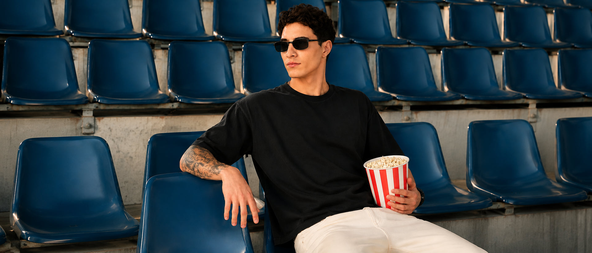 Model wearing YOURWAY oversized black plain t-shirt sitting in stadium seats during a streetwear photoshoot