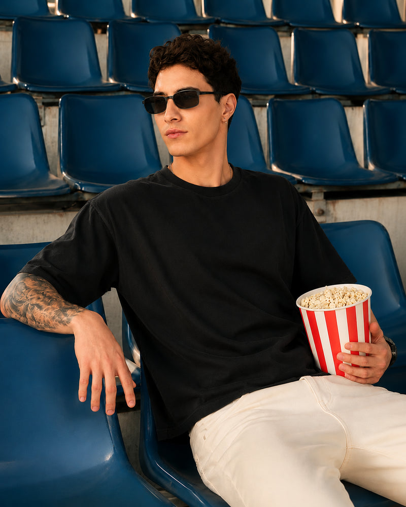 Model wearing YOURWAY oversized black plain t-shirt sitting in stadium seats during a streetwear photoshoot